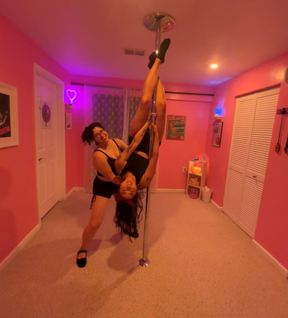 dahlia helping a pole student perform an inverted hang